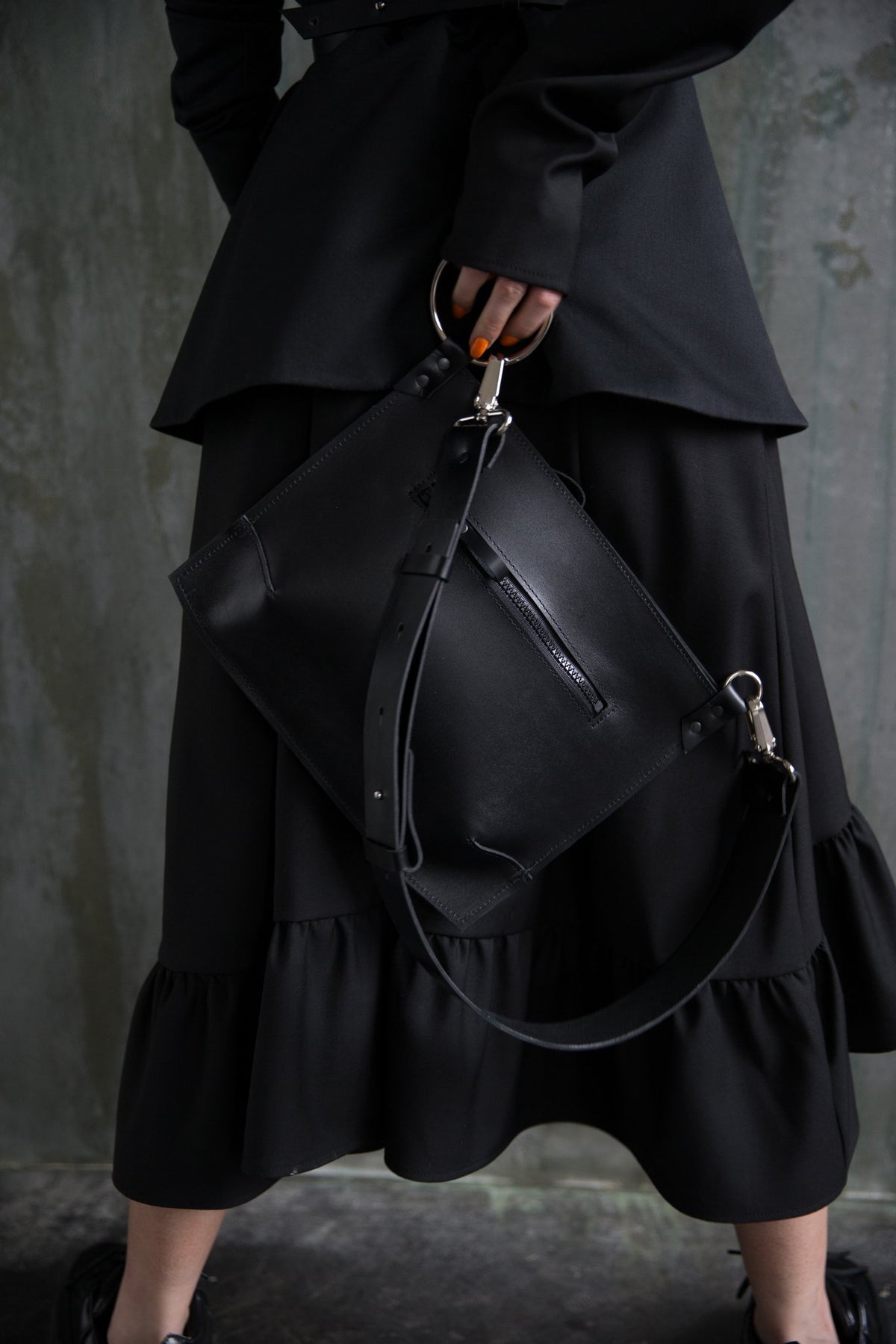 1. Woman holding PYKOK Serenity black leather handbag with adjustable strap, styled with black outfit