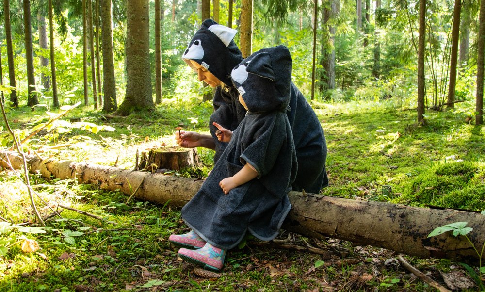 1. Kids wearing RÄTT Short-Sleeve Poncho WOLF in forest setting, showcasing hood and cozy design