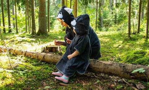 1. Kids wearing RÄTT Short-Sleeve Poncho WOLF in forest setting, showcasing hood and cozy design