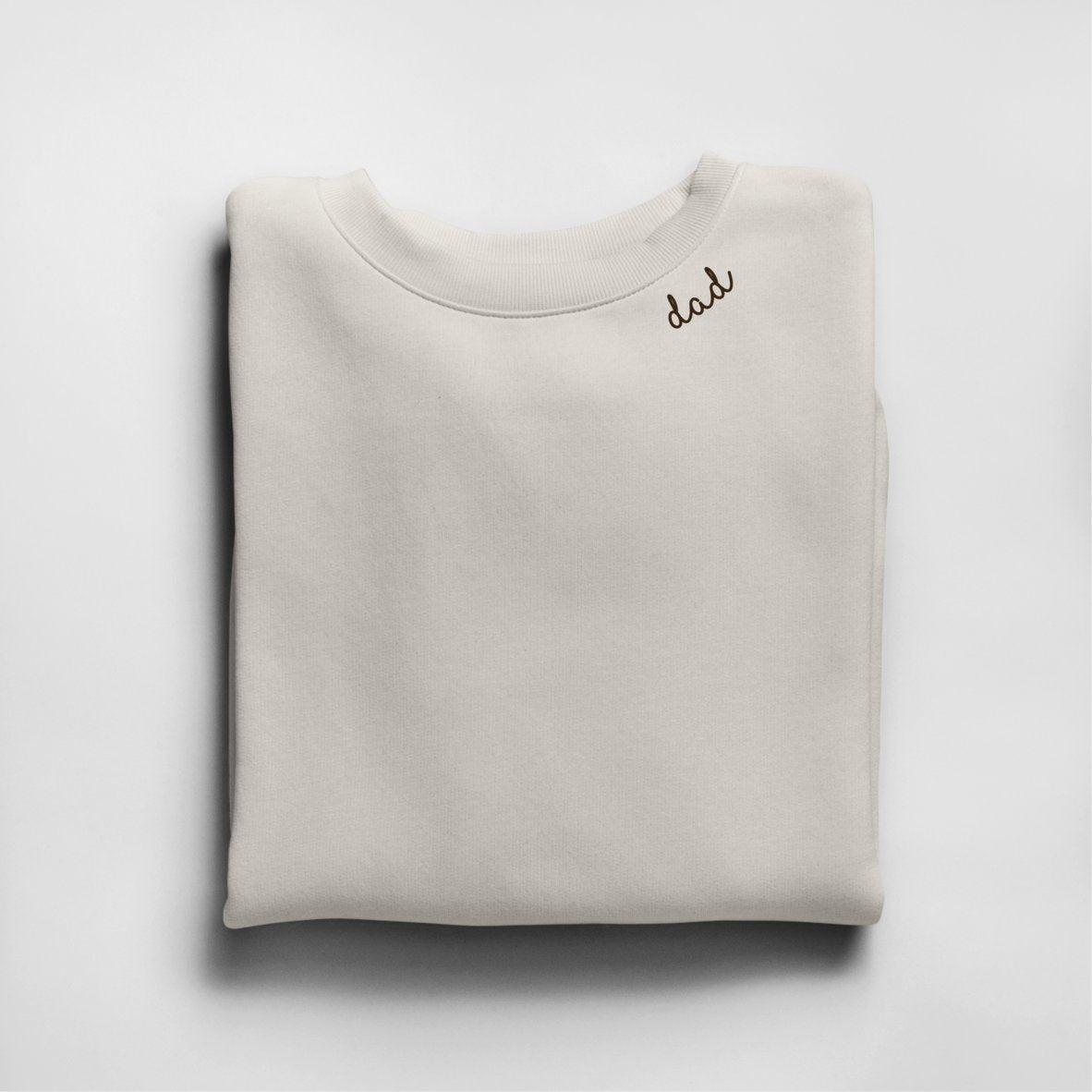 3. Beige unisex organic cotton sweatshirt with 'dad' embroidery, folded in studio setting