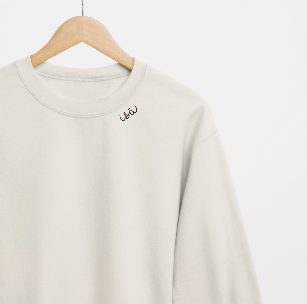 3. Beige organic cotton sweatshirt with 'Isä' embroidery on hanger in studio setting