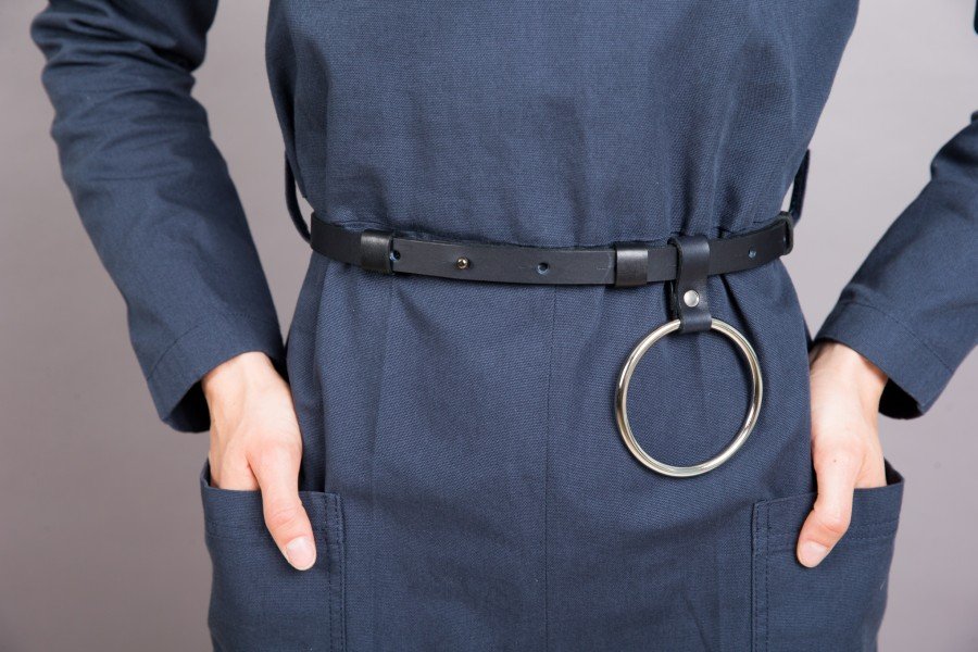 3. Close-up of women's black leather belt with metal O ring by PYKOK, styled over a navy outfit