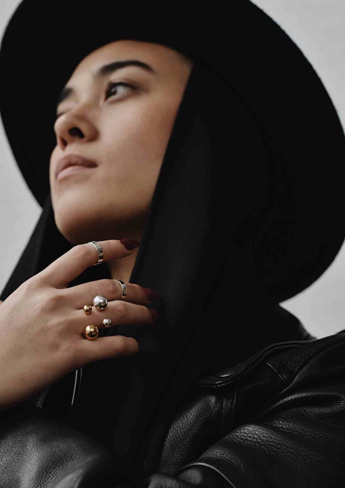 3. Woman wearing multiple NO MORE rings including Big Bomb Multisize Ring in gold, styled with a black hat and leather jacket