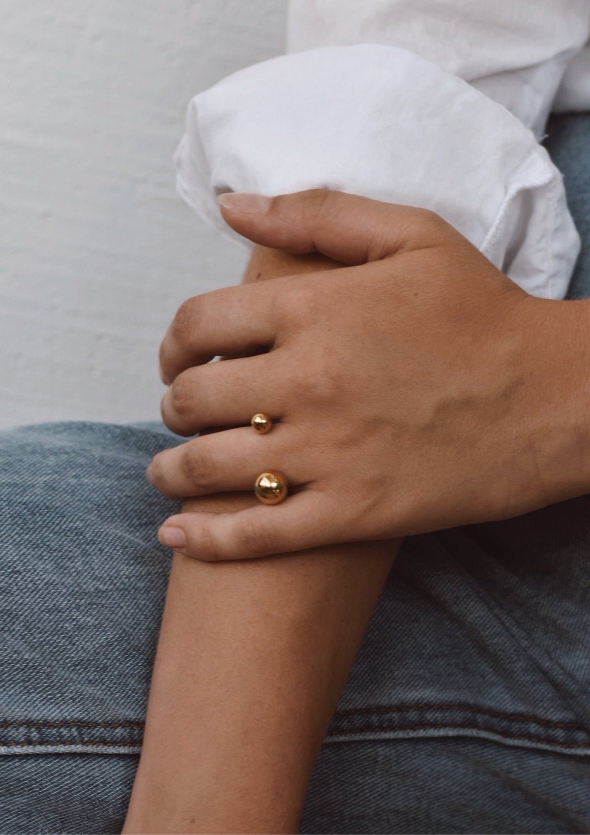9. Close-up of woman's hand wearing NO MORE Big Bomb Multisize Ring in gold, styled with a white shirt and jeans
