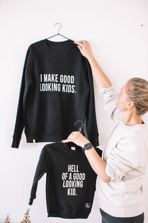 5. Flat lay of Black Giraffe Brand matching black sweatshirts for dad and child, featuring 'I Make Good Looking Kids' and 'Hell of a Good Looking Kid' text, displayed on hangers