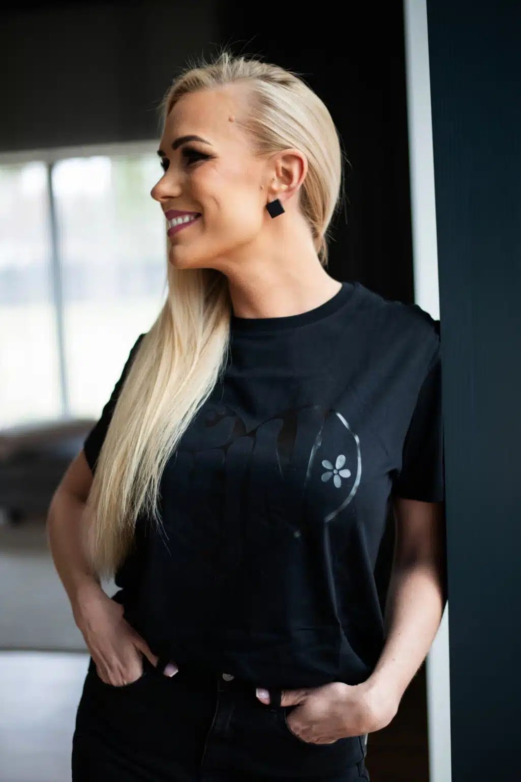 1. Woman wearing Black Giraffe Brand Be Kind T-shirt in black with subtle black-on-black print, shown in lifestyle setting