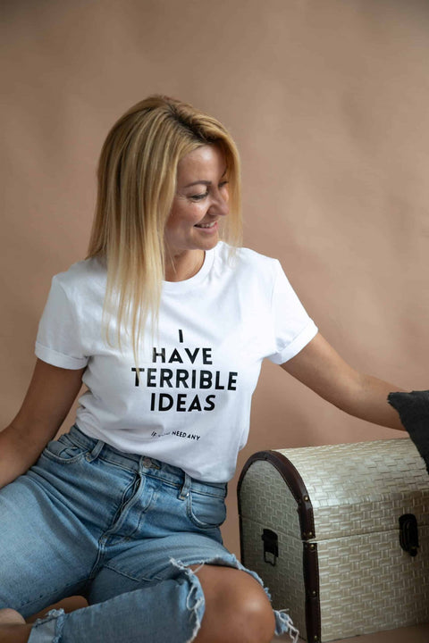 1. Women's white 'I Have Terrible Ideas' t-shirt by Black Giraffe Brand, styled with rolled-up sleeves, worn by model sitting casually