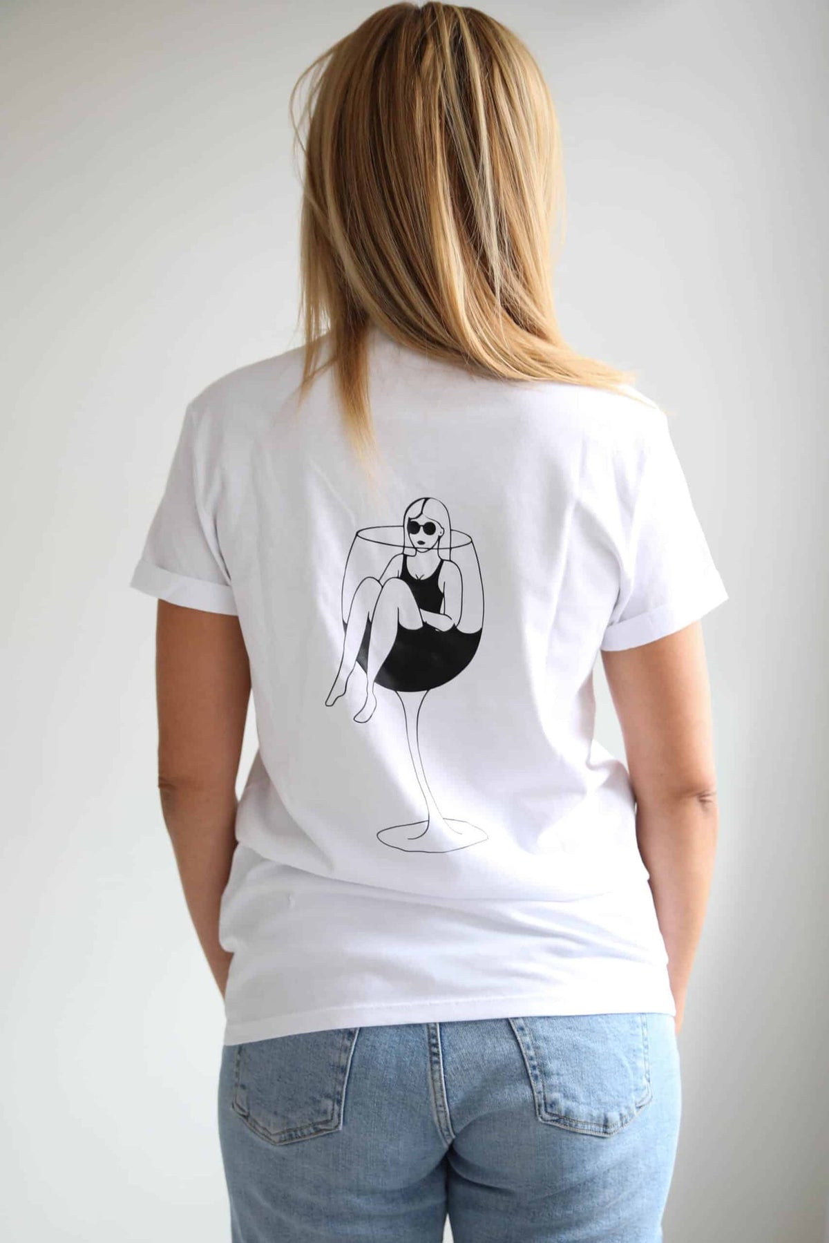 3. Back view of women's white T-shirt by Black Giraffe Brand, featuring wine glass illustration, shown in studio