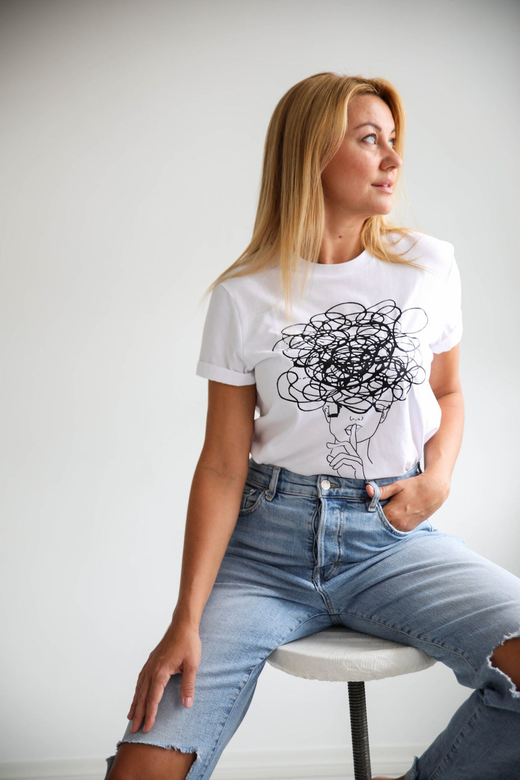 3. Women's white Šššhhh! T-shirt by Black Giraffe Brand featuring abstract face design, shown with rolled-up sleeves in studio