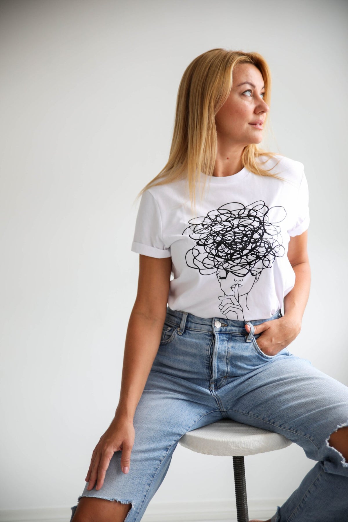3. Women's white Šššhhh! T-shirt by Black Giraffe Brand featuring abstract face design, shown with rolled-up sleeves in studio