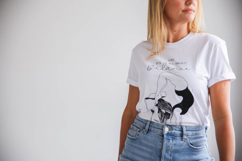2. Women's white 'It's All About Balance' T-shirt by Black Giraffe Brand, shown in a studio setting with rolled-up sleeves