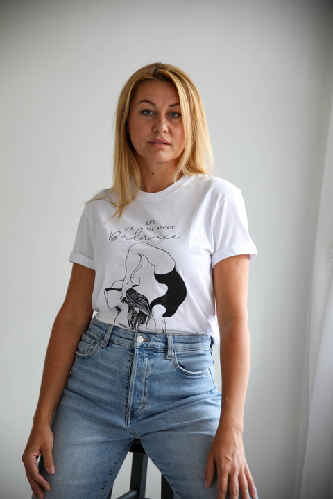 1. Women's white 'It's All About Balance' T-shirt by Black Giraffe Brand, worn with rolled-up sleeves and light denim jeans in a lifestyle setting