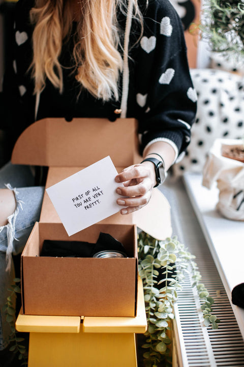 2. Woman opening Black Giraffe Body Care Gift Set, revealing a card with a positive message