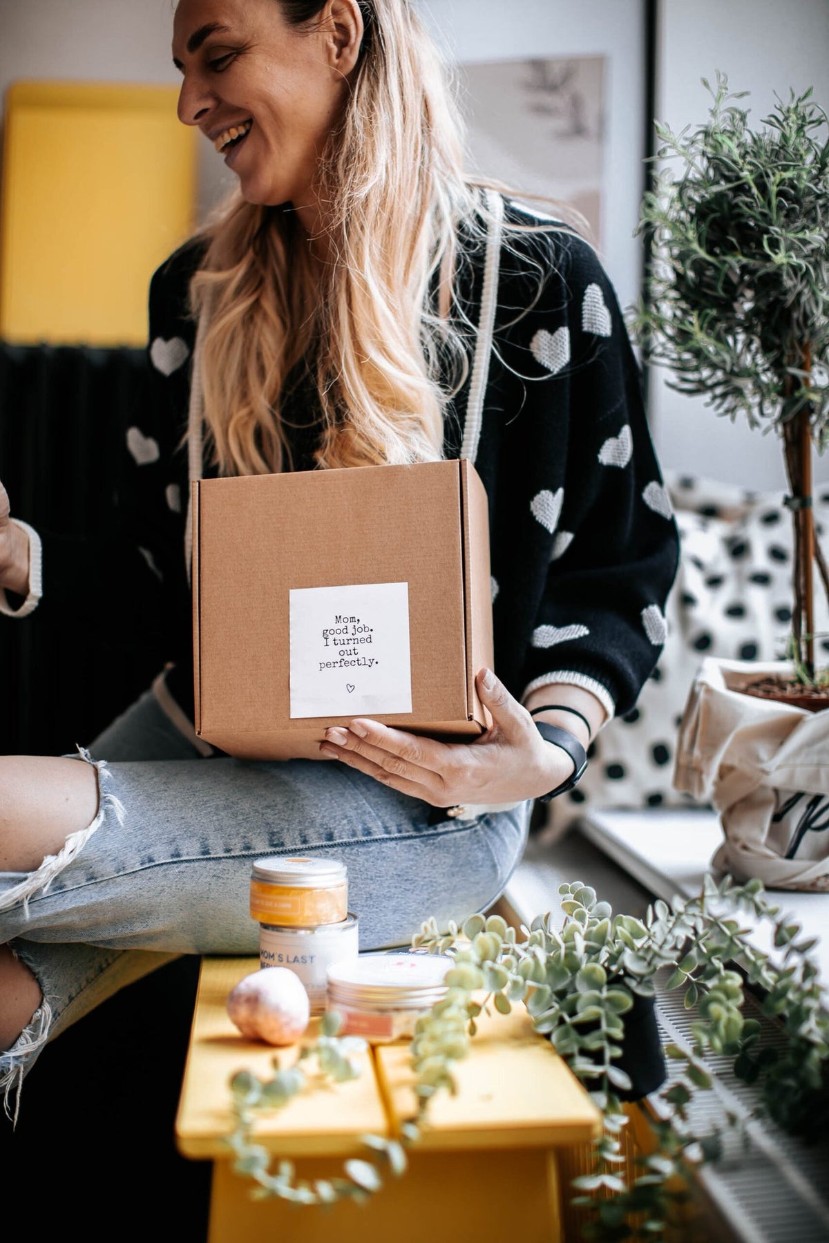 1. Woman holding Black Giraffe Body Care Gift Set box, featuring heart-patterned sweater and casual setting