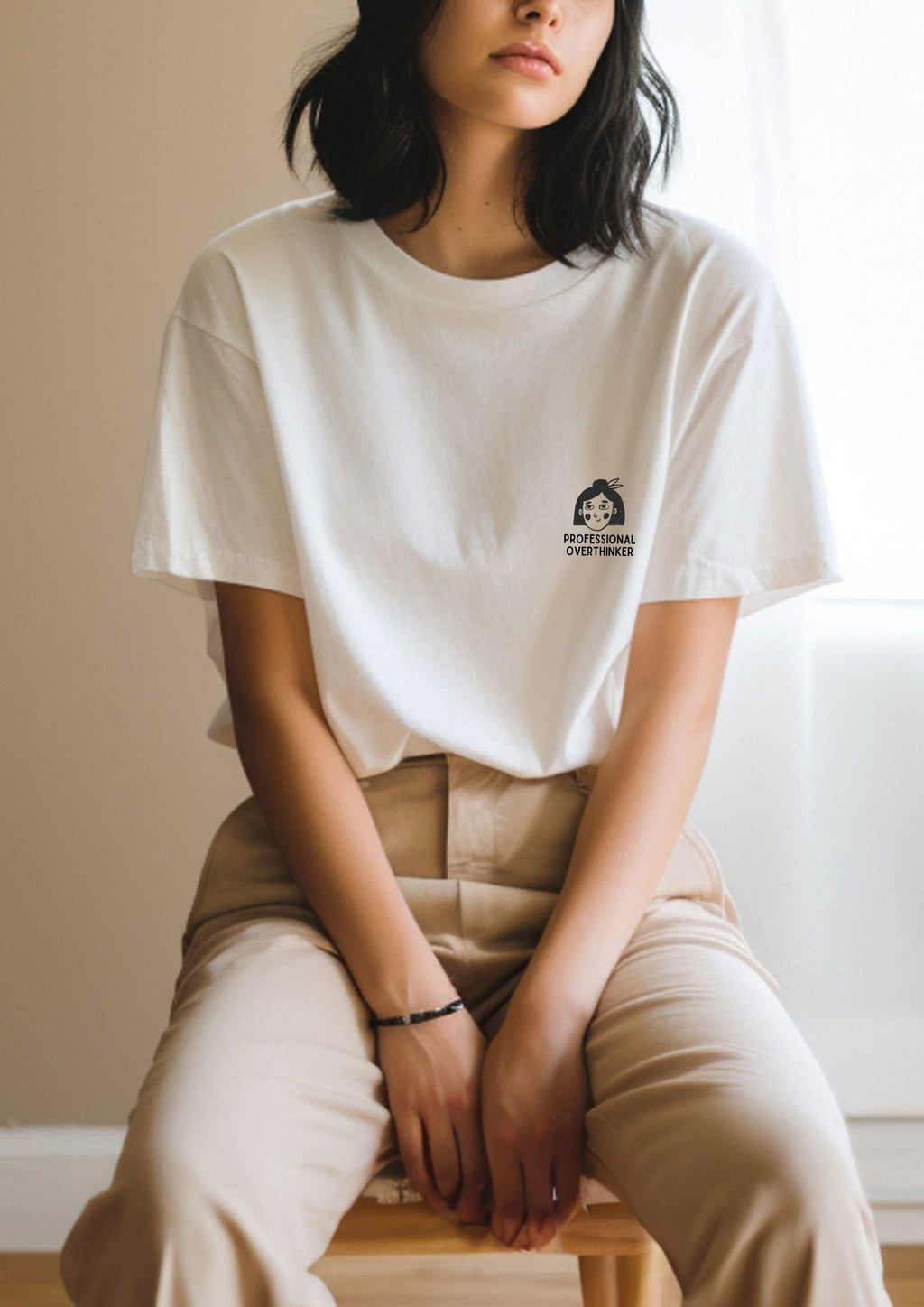3. Women's white Professional Overthinker T-shirt by Black Giraffe Brand, styled with beige pants, shown in a relaxed indoor setting