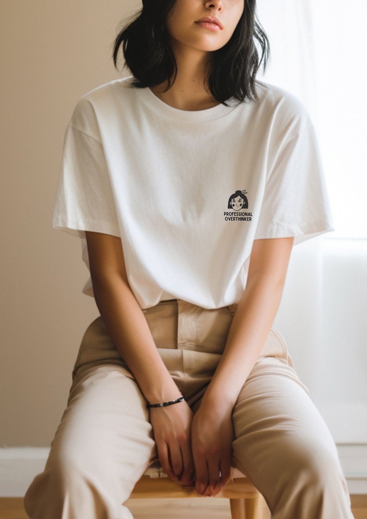 3. Women's white Professional Overthinker T-shirt by Black Giraffe Brand, styled with beige pants, shown in a relaxed indoor setting