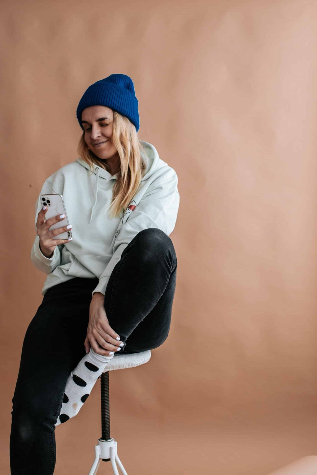 1. Woman wearing Black Giraffe Brand 'Aged Like Fine Wine' hoodie in light green, sitting on stool, lifestyle setting