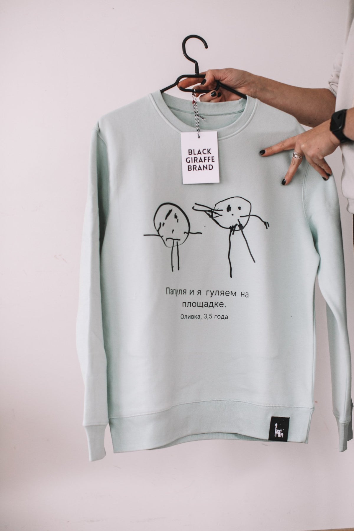 5. Sage green sweatshirt with child's drawing, Black Giraffe Brand, displayed in studio