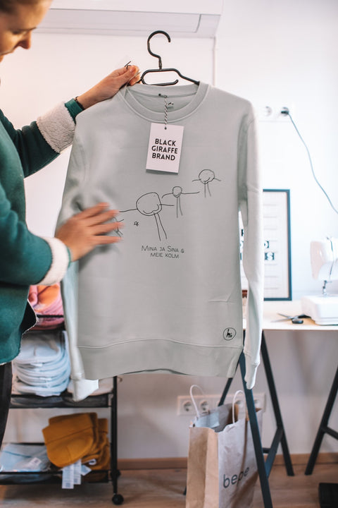 3. Sage green sweatshirt featuring child's artwork, Black Giraffe Brand, held in studio setting