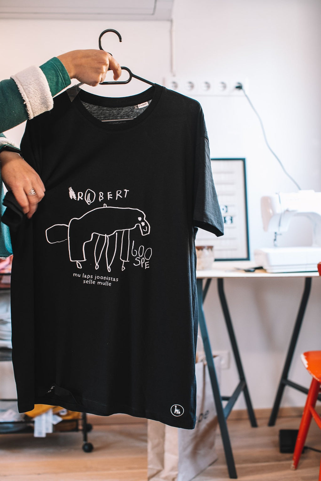 2. Black Giraffe Brand black T-shirt featuring child's drawing of an animal with text, held by a person in a casual setting
