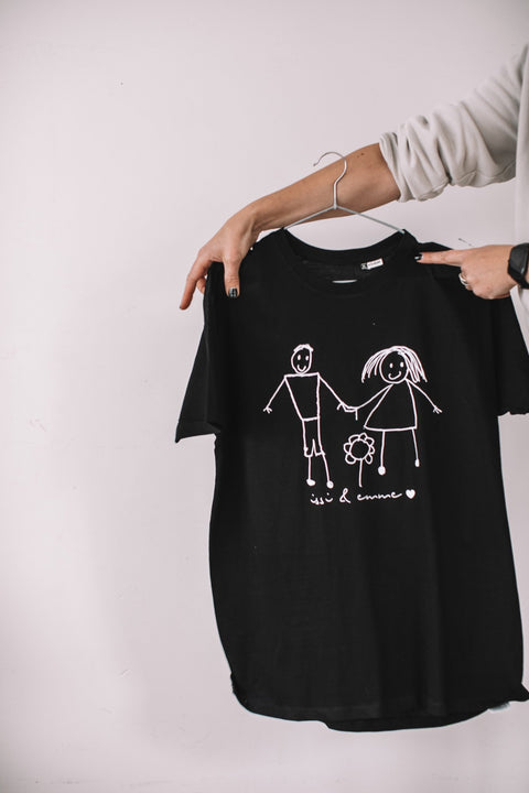 5. Black Giraffe Brand black T-shirt with child's drawing of a family, held by a person in a casual setting