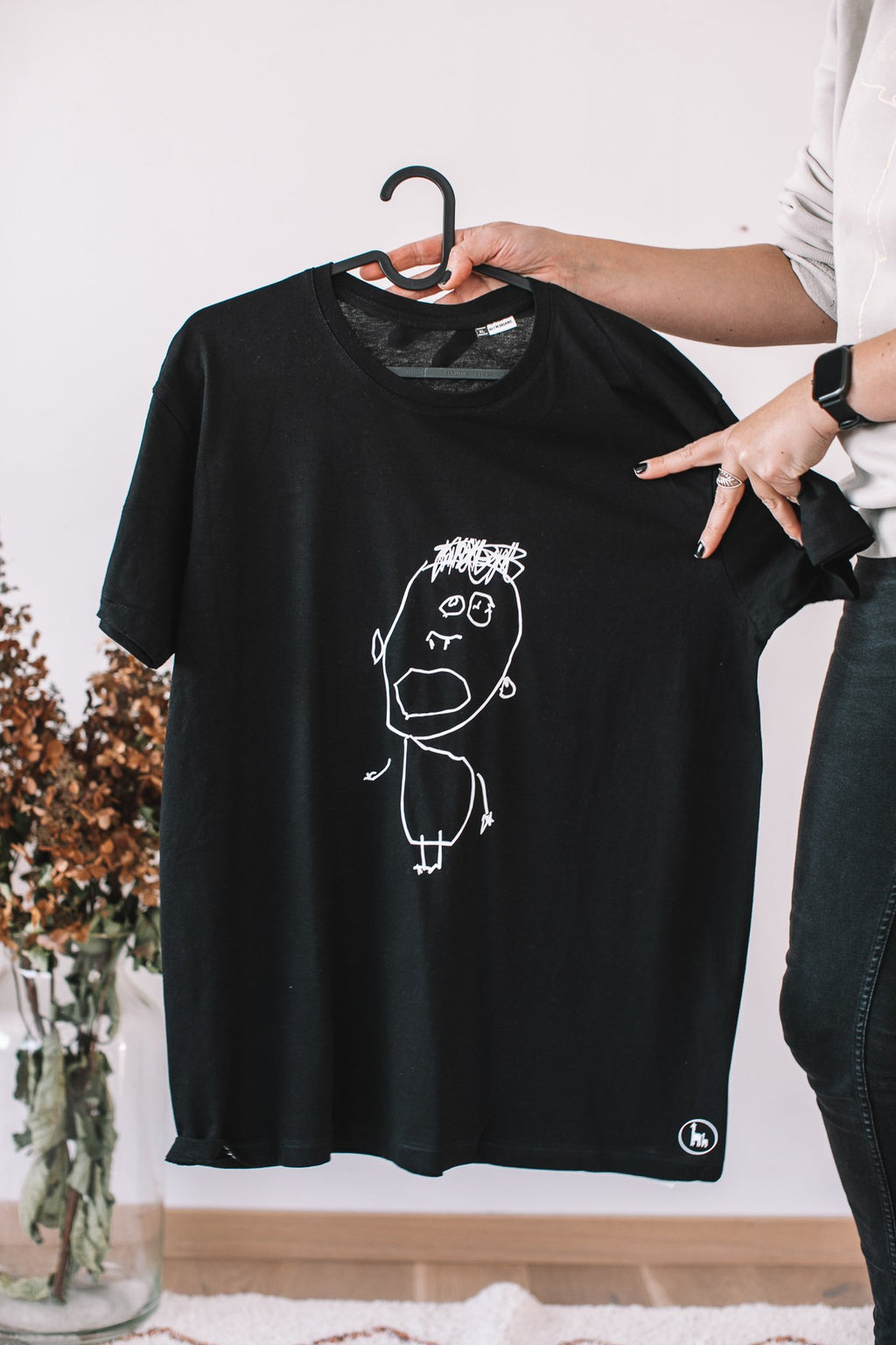 4. Black Giraffe Brand black T-shirt featuring child's drawing of a face, held by a person in a casual setting