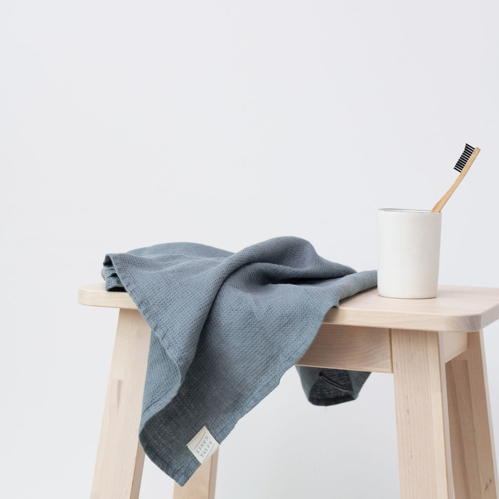 3. Blue fog linen fine waffle towel draped over wooden stool with toothbrush in cup, modern bathroom style