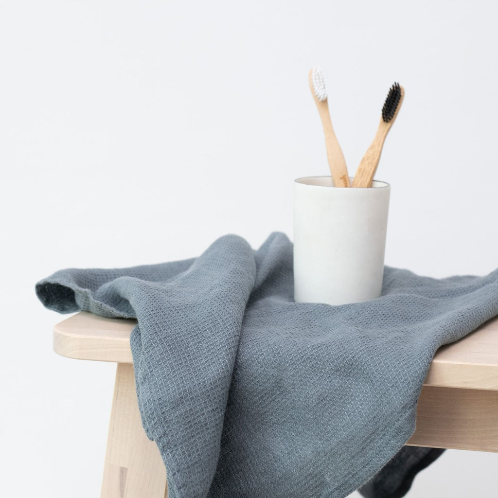 3. Blue fog waffle linen towel draped over a stool with a cup holding two bamboo toothbrushes