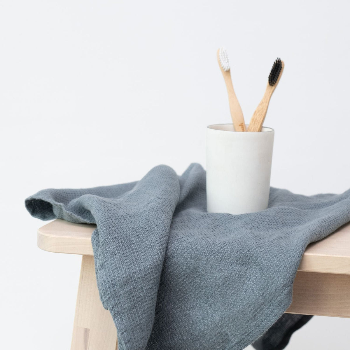 3. Blue fog waffle linen towel draped over a stool with a cup holding two bamboo toothbrushes