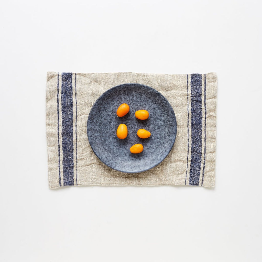 1. Blue vintage stripe linen placemat with a grey plate and kumquats on a white background