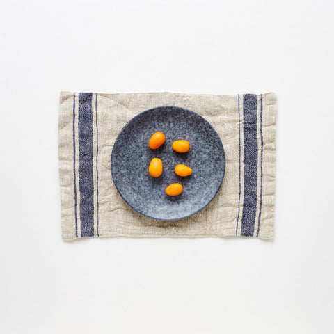 1. Blue vintage stripe linen placemat with a grey plate and kumquats on a white background