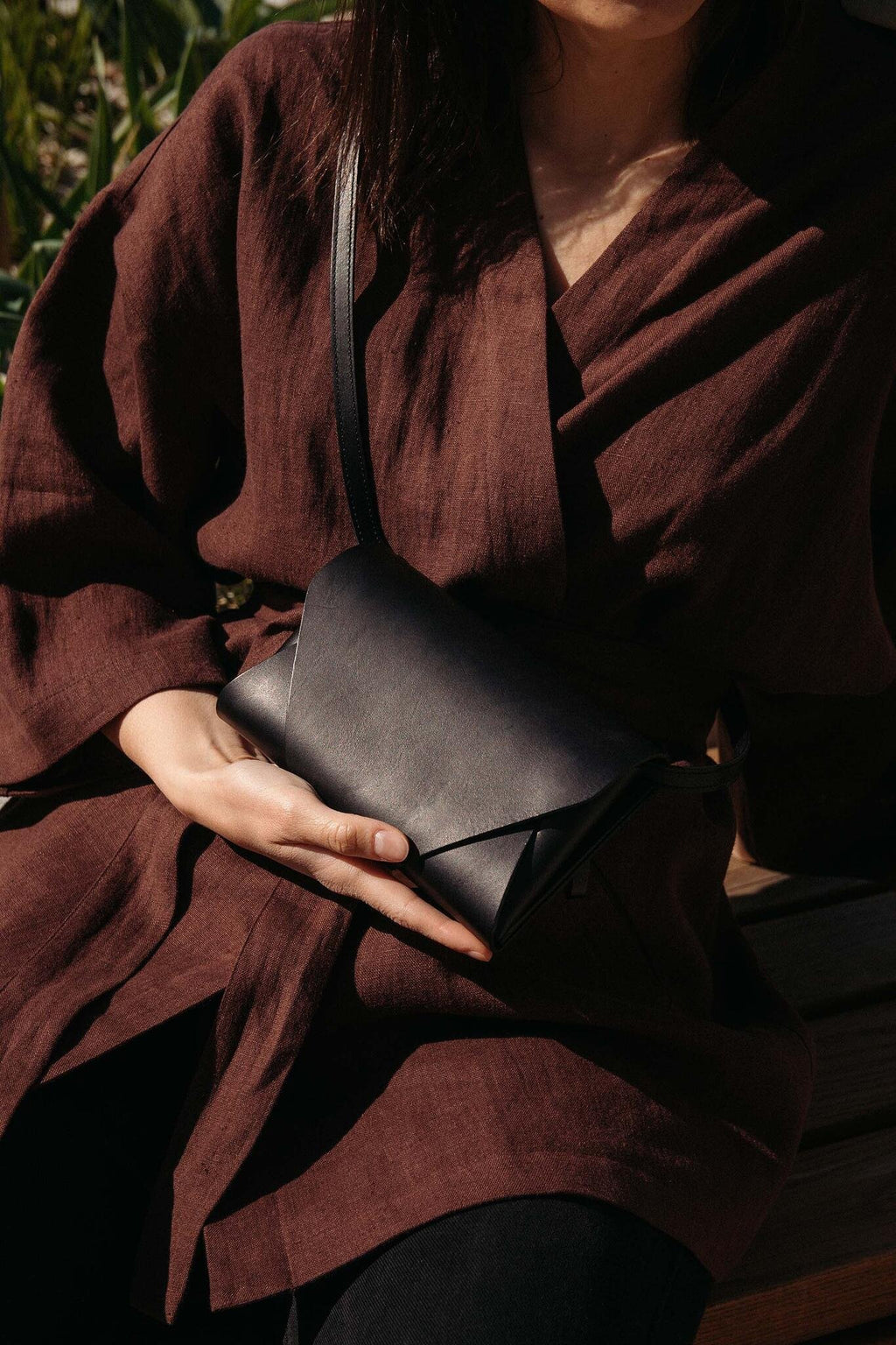 1. Woman holding black leather Stella Soomlais Capital of Plenty clutch-wallet in outdoor setting