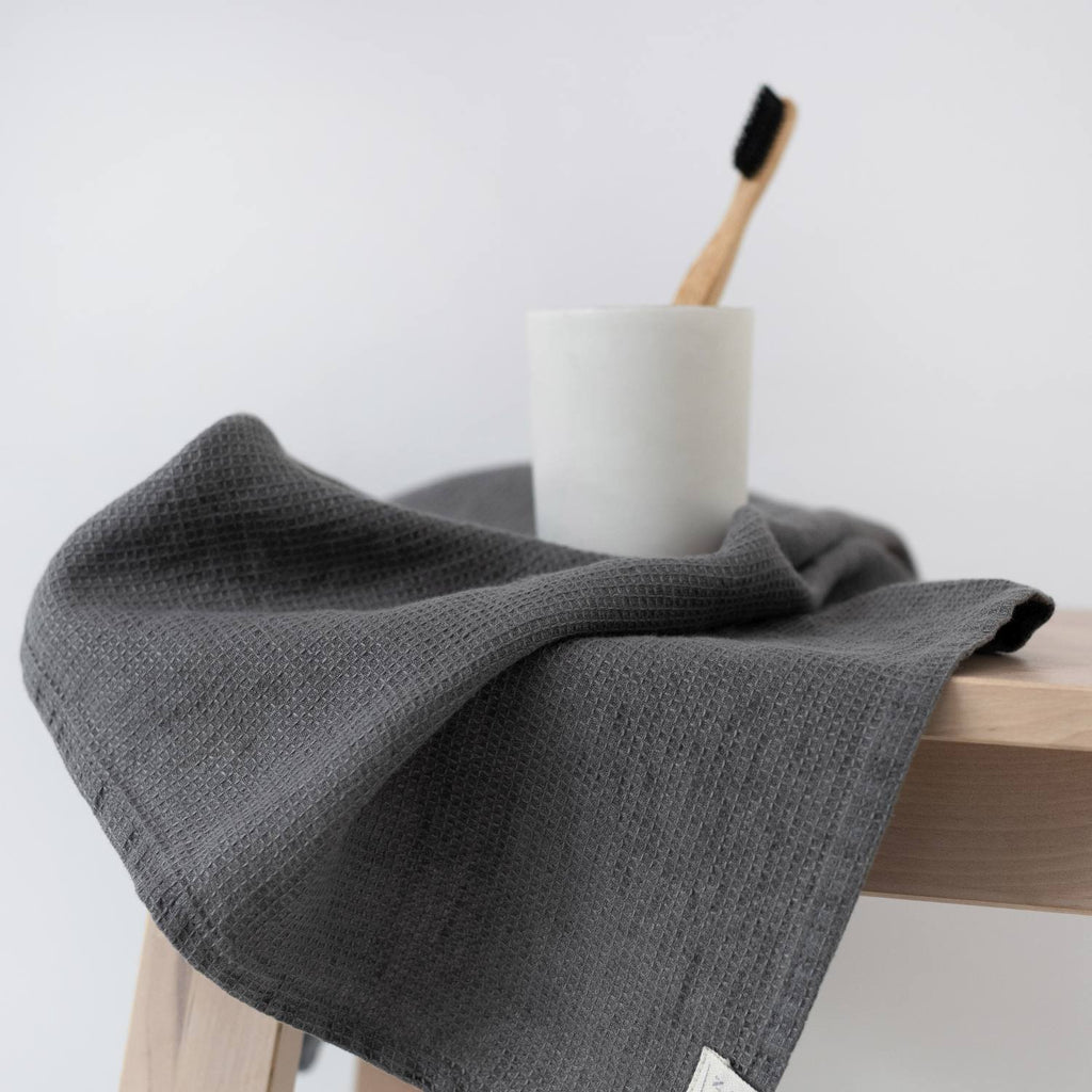 2. Charcoal waffle linen towel draped over a wooden stool with a toothbrush and cup, simple bathroom decor