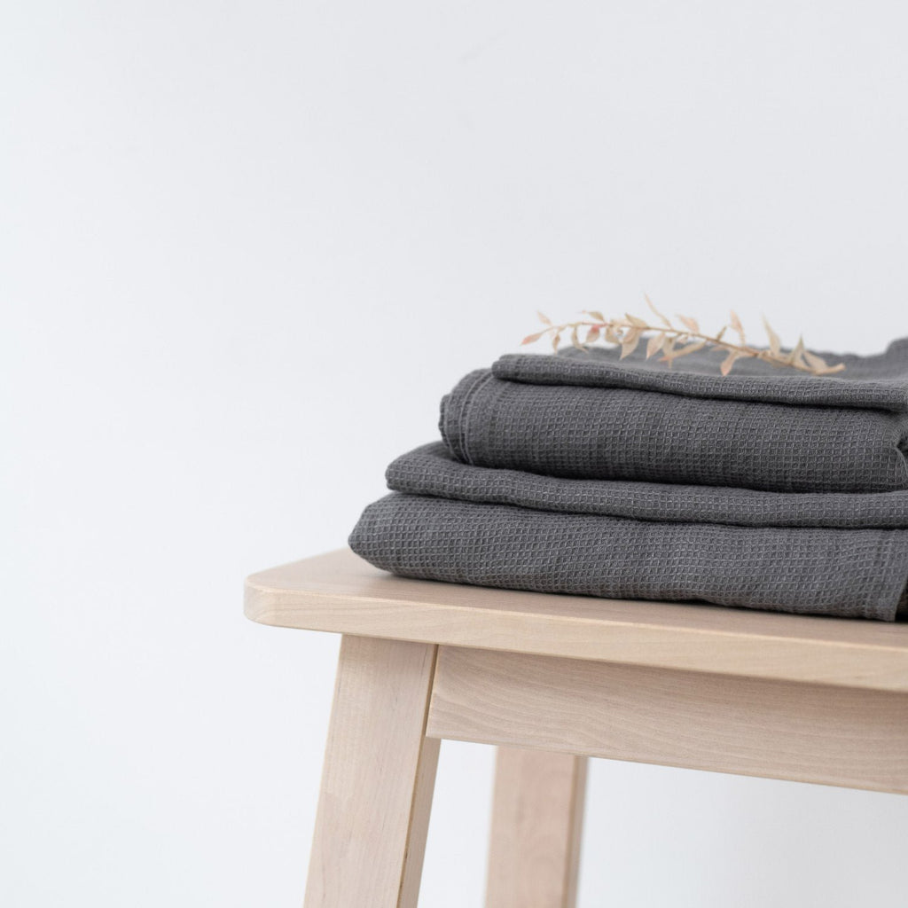 3. Neatly folded charcoal waffle linen towels on a wooden stool with decorative dried flowers, minimalist style