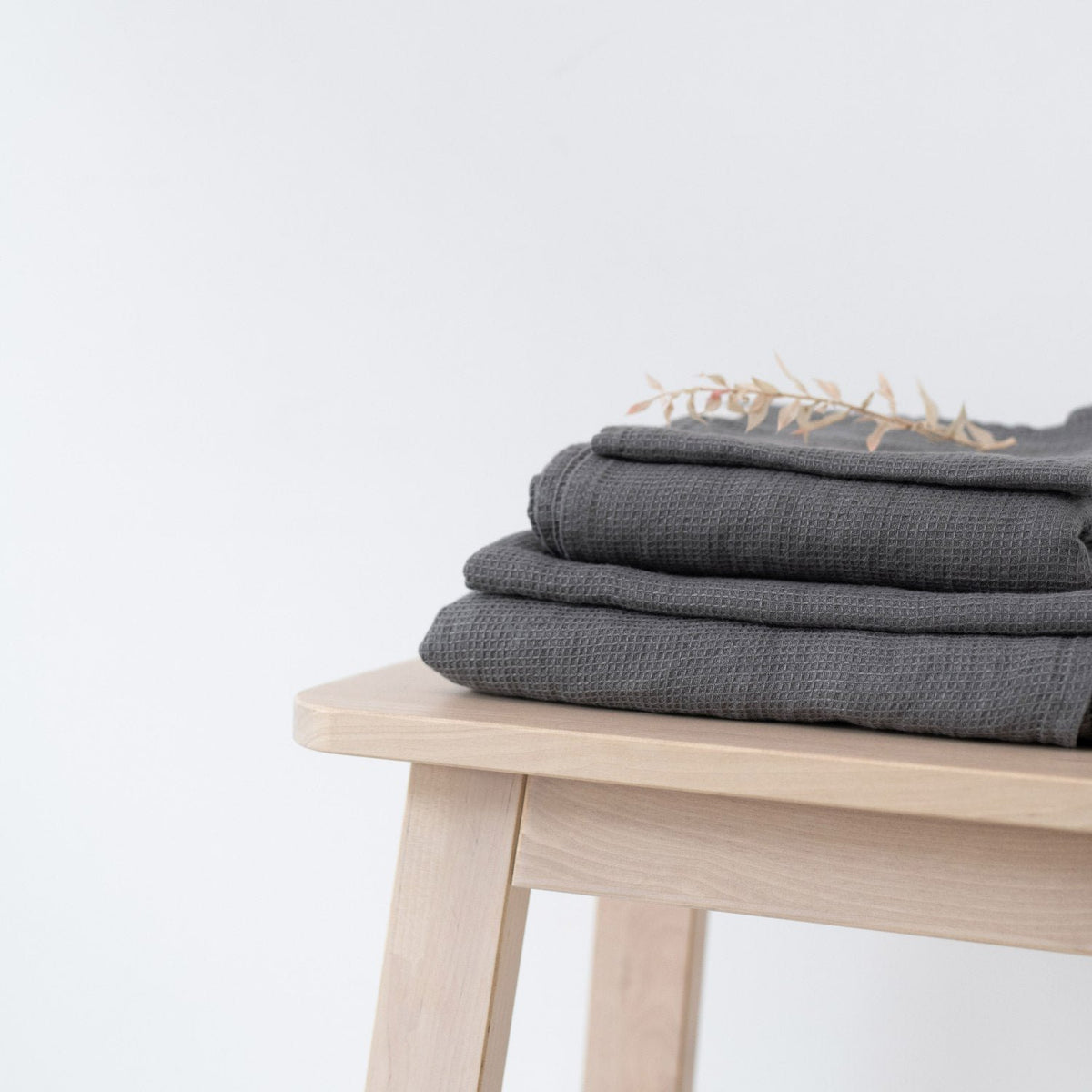 3. Neatly folded charcoal waffle linen towels on a wooden stool with decorative dried flowers, minimalist style