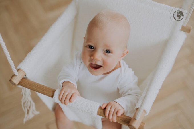 5. Baby smiling in bouclé snow white swing with oak wood poles, looking up in a bright room