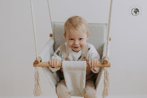 2. Child sitting in Nofi KIDS bouclé ice grey swing with oak wood poles, smiling indoors