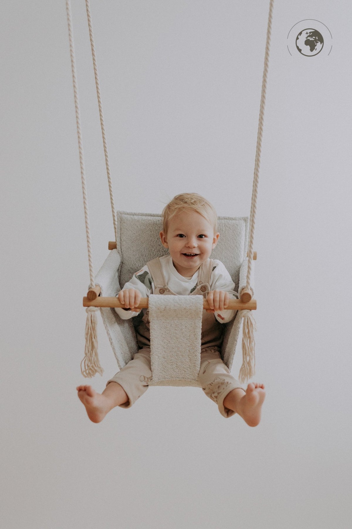 1. Smiling child sitting in Nofi KIDS bouclé ice grey baby swing with oak wood poles indoors