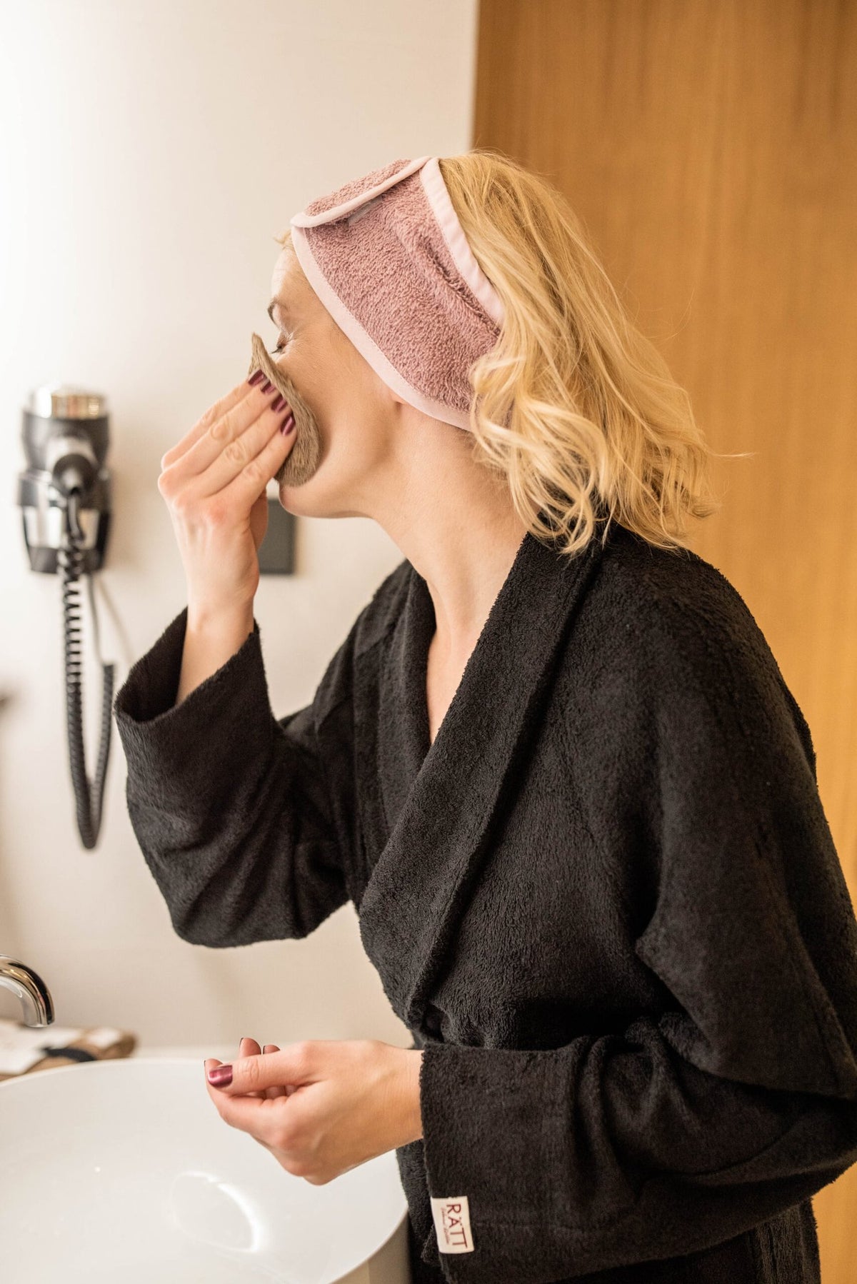 2. Woman using RÄTT cotton terry headband in bathroom setting, highlighting practical use