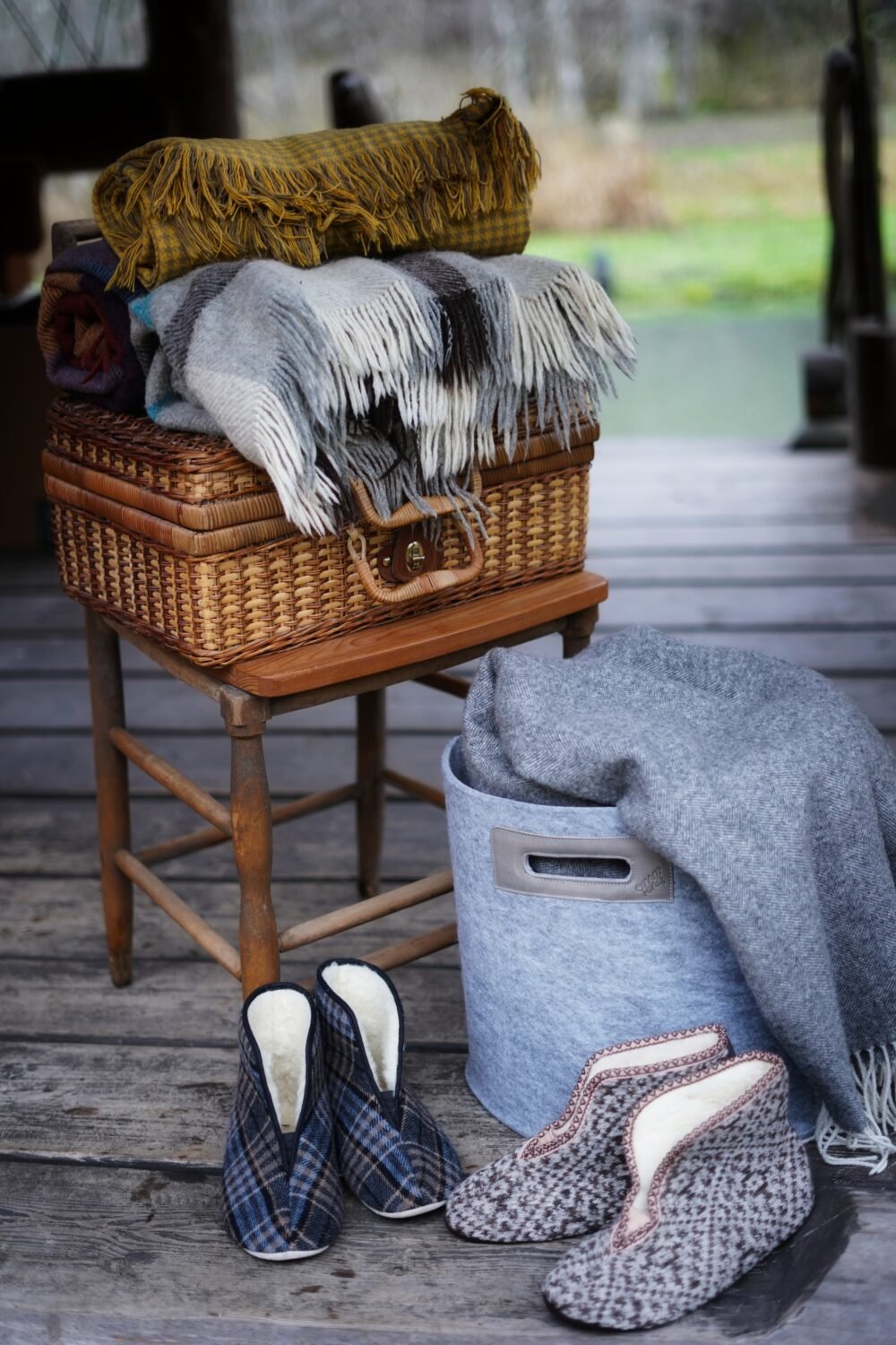 1. Lifestyle image of Omaking Trolla lambswool slippers in beige, styled with cozy blankets on a rustic porch