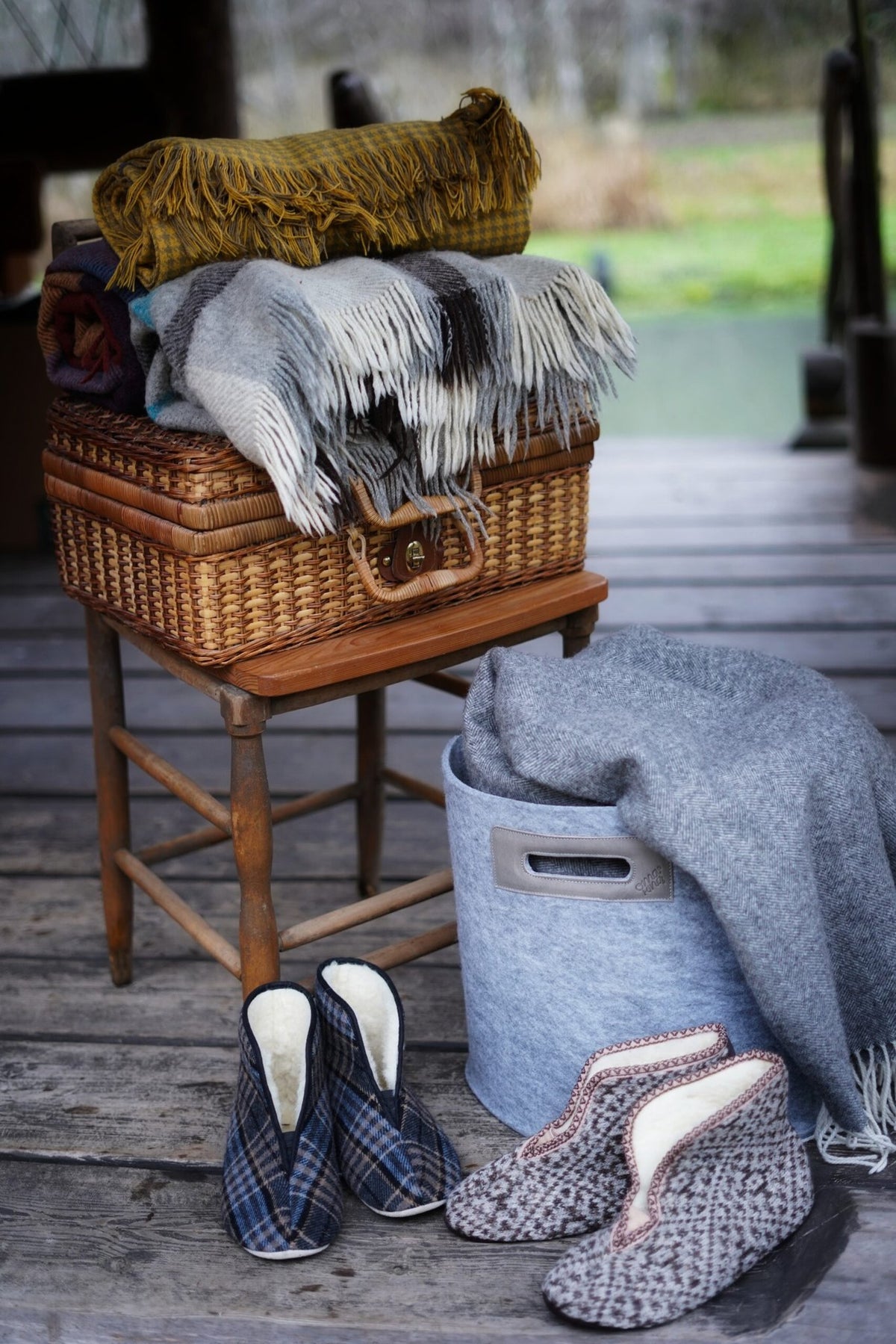 1. Lifestyle image of Omaking Trolla Lambswool Slippers in plaid pattern, styled with cozy blankets on a wooden porch
