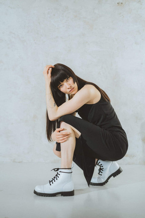 1. Woman sitting on chair wearing Samelin 517 Aviator Boots in white, styled with a black dress, showcasing urban fashion
