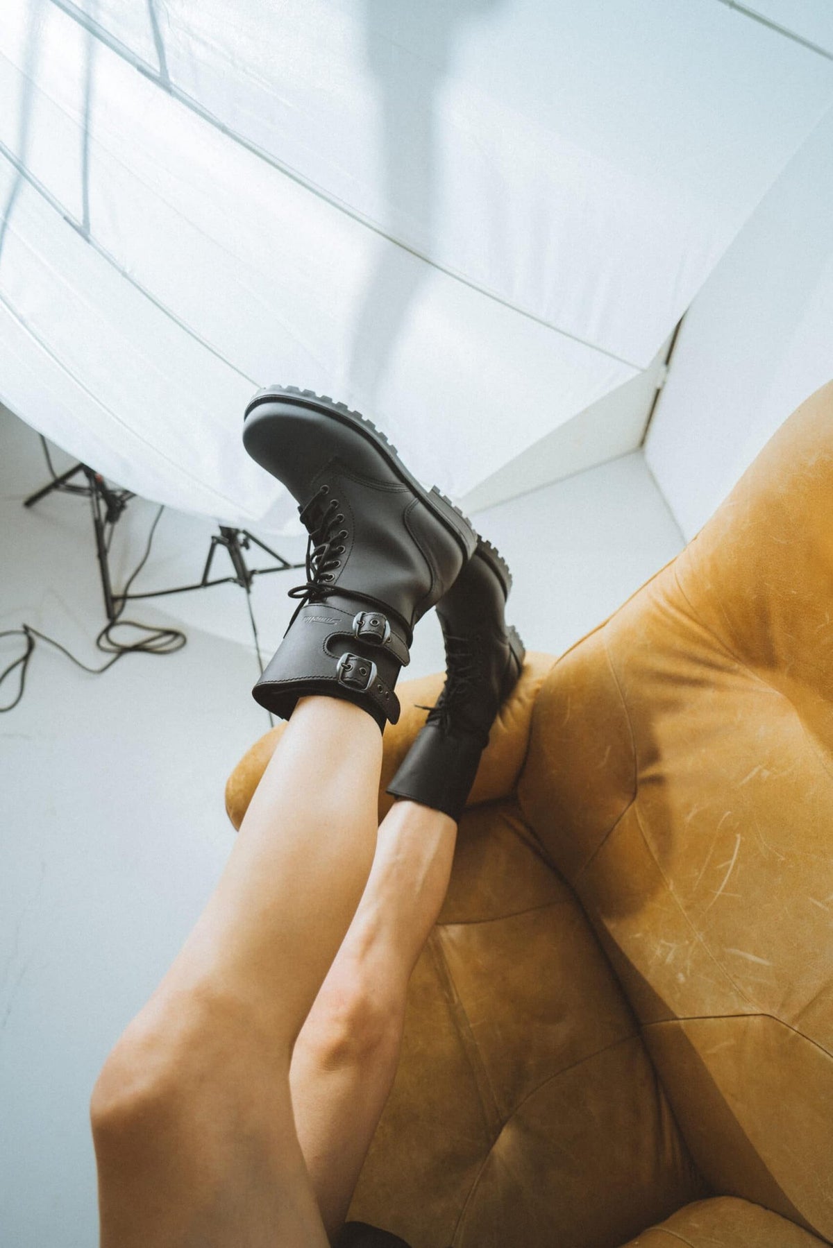 1. Unisex black Tarkovsky boots by Samelin worn by a model on a brown couch in a lifestyle setting