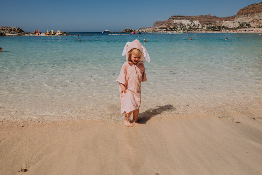 8. Child in pink RÄTT short-sleeve poncho with hood, standing on the beach