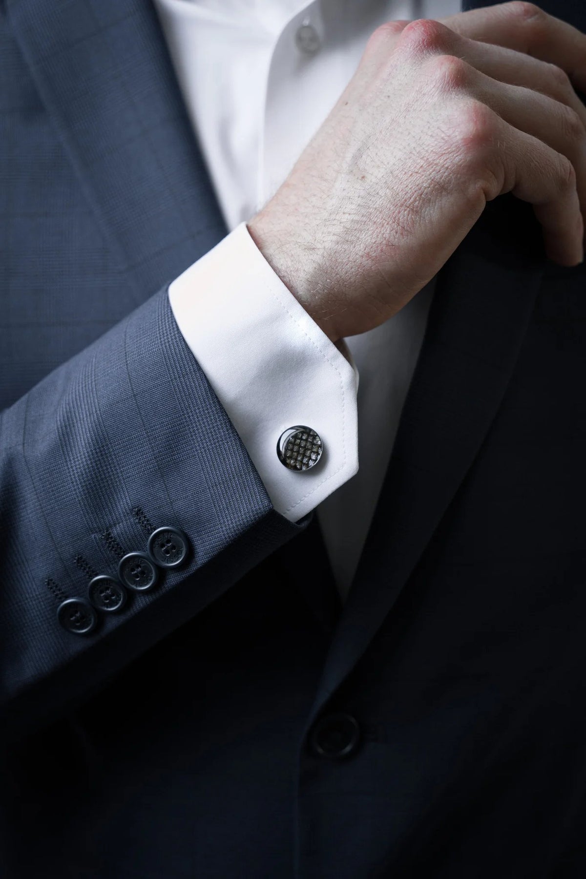 1. Man wearing dark suit with white shirt showcasing Eherüs round cufflinks made from brown trout leather