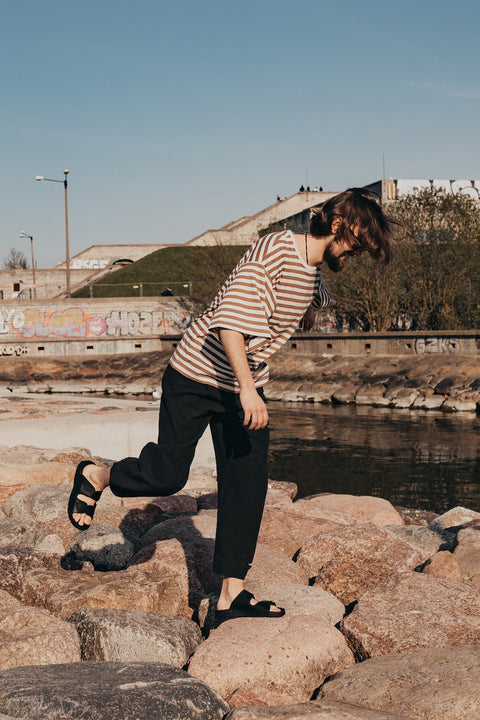 1. Men's Madise Sandals in black worn by a model on rocky terrain, showcasing outdoor versatility