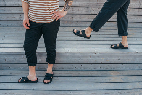3. Men's black Märt Sandals by Omaking worn by two models on wooden steps, emphasizing casual style