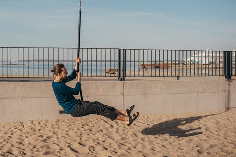 4. Men's black Märt Sandals by Omaking worn by a model swinging on a beach, highlighting outdoor versatility