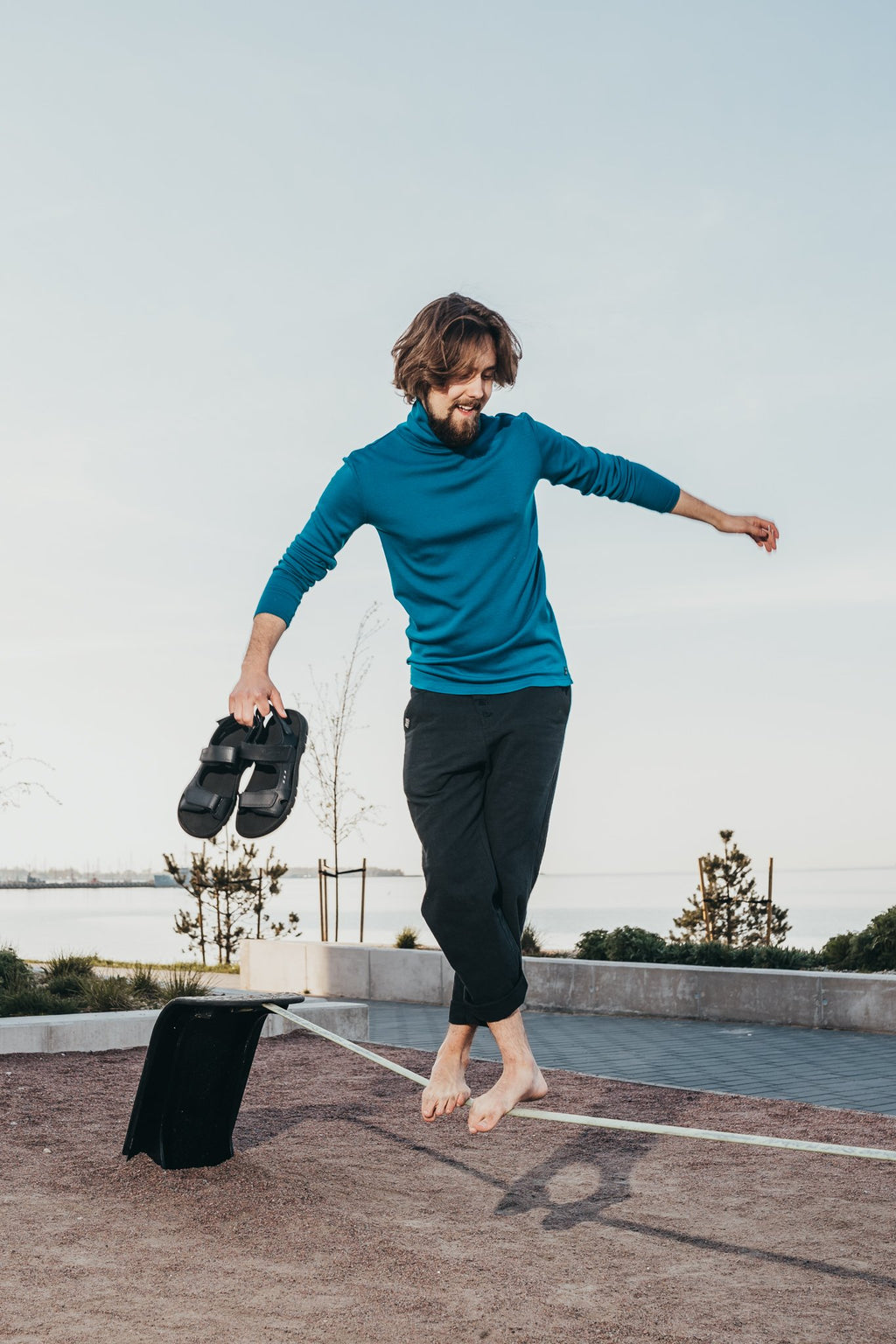 1. Man balancing on a slackline holding Omaking Lauri Leather Sandals in brown, showcasing outdoor versatility
