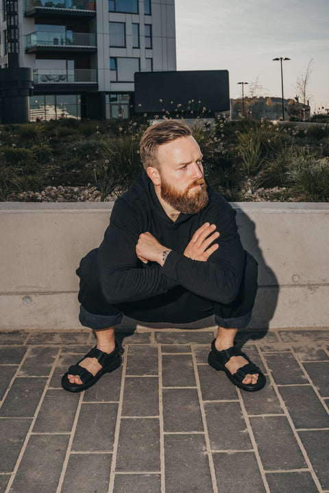 2. Man squatting on pavement wearing Omaking Lauri Leather Sandals in brown, highlighting comfort and style